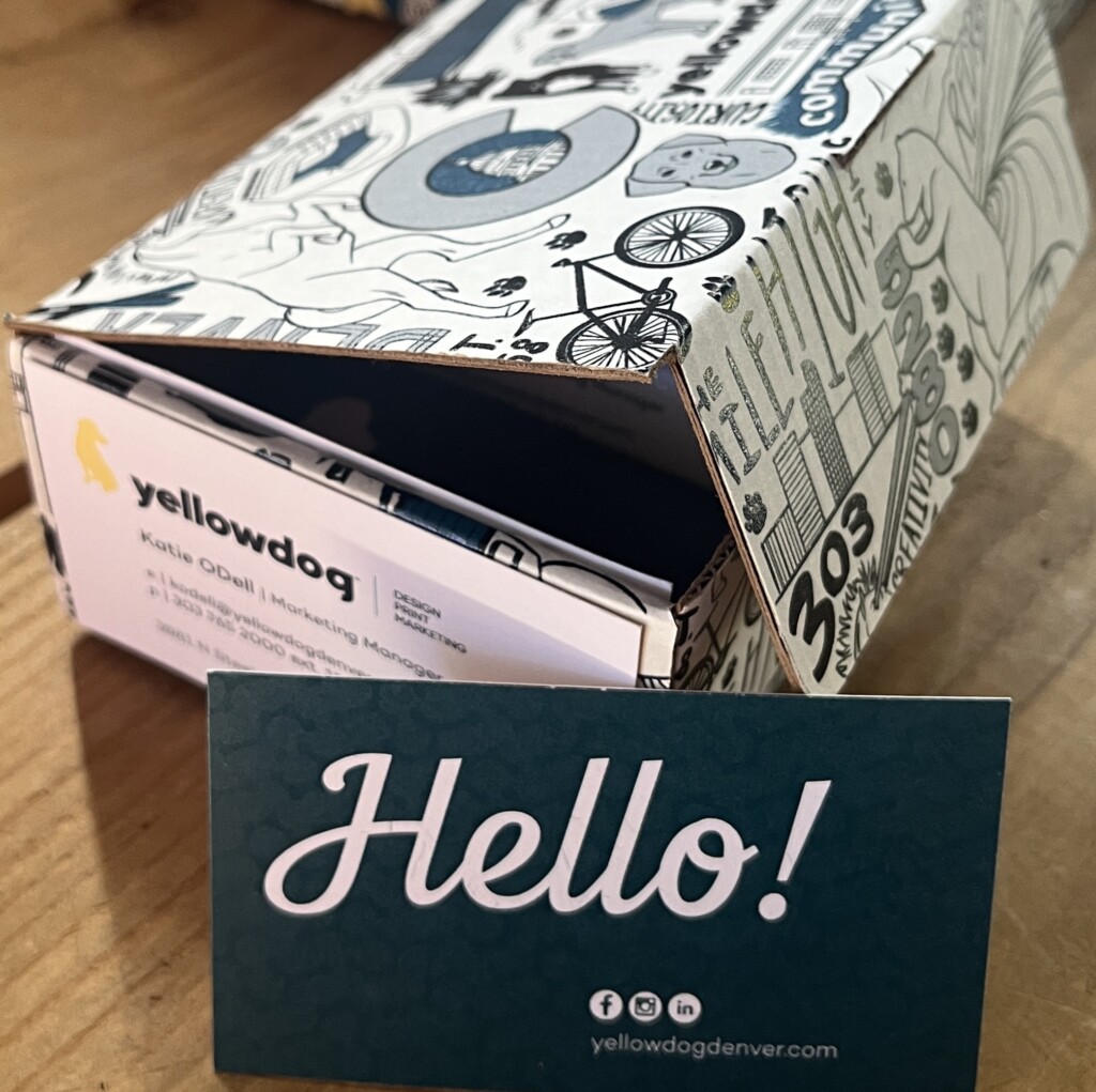 A business card with the word "Hello!" in cursive is pictured leaning against a pattern-printed box.